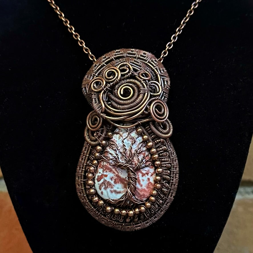 A detailed close-up of a handmade copper wire wrapped crazy lace aget tree of life pendant necklace on a black display bust. 