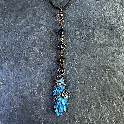 A handmade copper wire-wrapped kyanite necklace featuring iridescent beads, displayed on a textured gray slate surface.